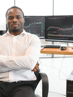 African American trader works at computer with displayed real-time stocks.