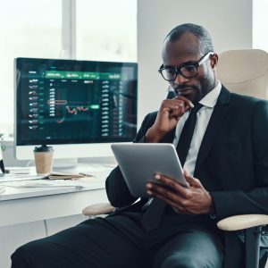 Concentrated young African man in formalwear using modern technologies while working in the office